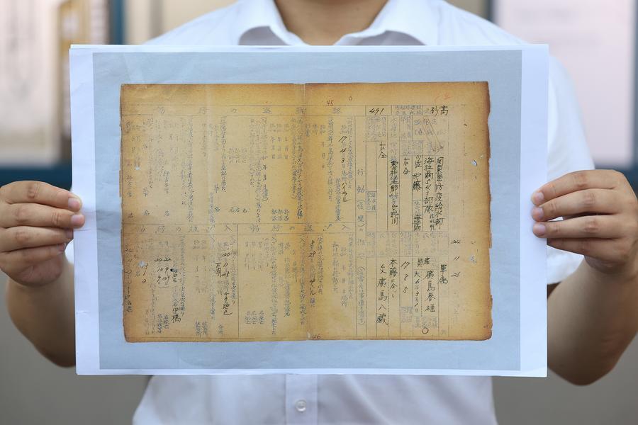 한 연구원이 12일 옛 731부대 하이라얼지대(만주 제543부대)의 '신상신고서' 문서 일부를 들어 보이고 있다. (사진/신화통신)