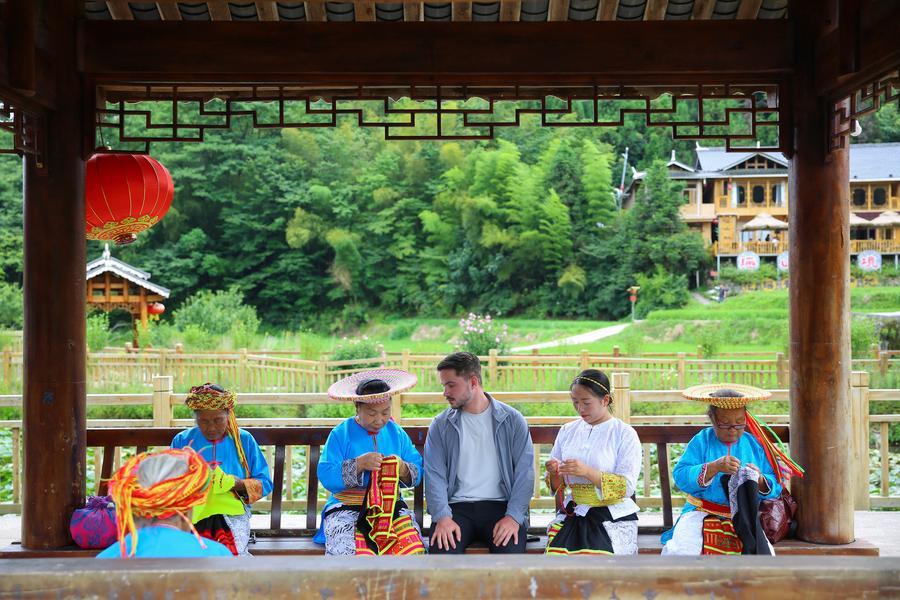 외국인 관광객들이 지난 4일 후난(湖南)성 룽후이(隆回)현 후싱산(虎形山) 야오(瑤)족향에서 화야오(花瑤) 여성들이 국가급 무형문화유산인 화야오 탸오화(挑花∙후난성 전통 자수)를 만드는 모습을 지켜보고 있다. (사진/신화통신)